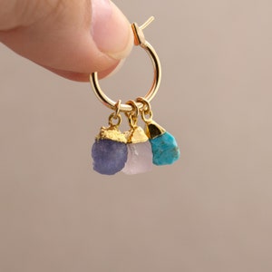 Op de afbeelding: Gouden creolen met drie hangende bedels: een paarse amethist, een roze rozenkwarts en een turquoise steen.