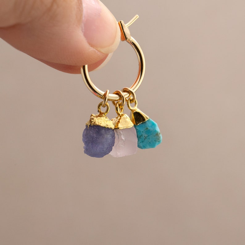 Op de afbeelding: Gouden creolen met drie hangende bedels: een paarse amethist, een roze rozenkwarts en een turquoise steen.