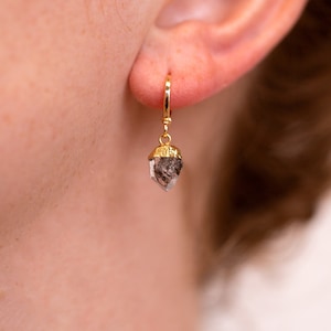 May include: Gold hoop earrings with a clear quartz crystal pendant. The crystal is faceted and has a gold-plated setting.