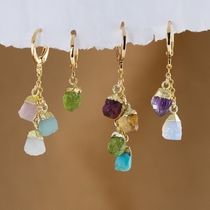 May include: Four pairs of gold earrings with different colored gemstone drops. Each earring features a variety of gemstone drops, including pink, blue, green, yellow, and purple.