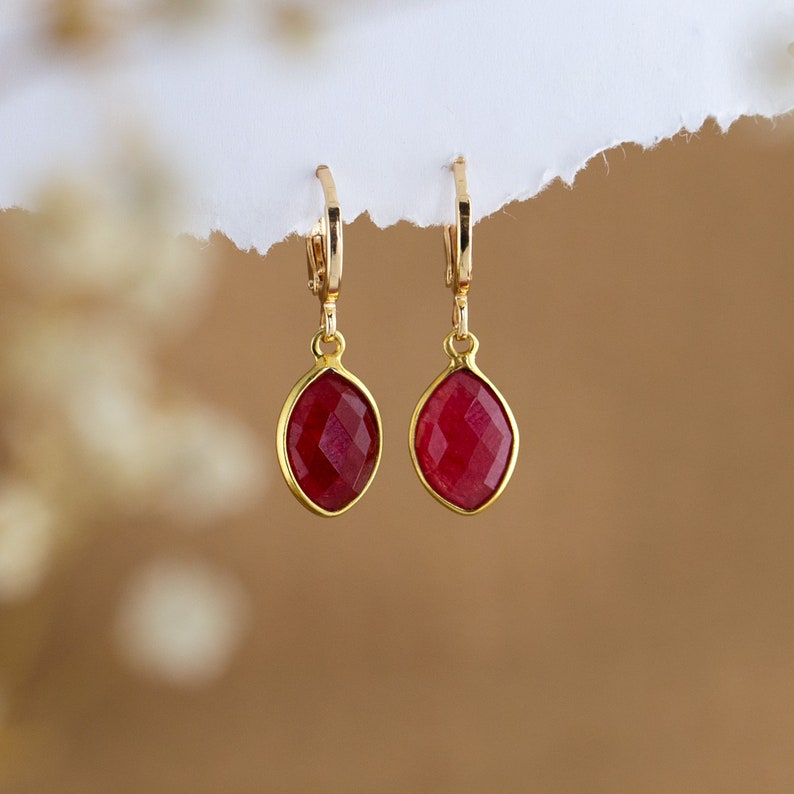 May include: A pair of gold earrings with red gemstone drops. The earrings have a simple design and are perfect for everyday wear.
