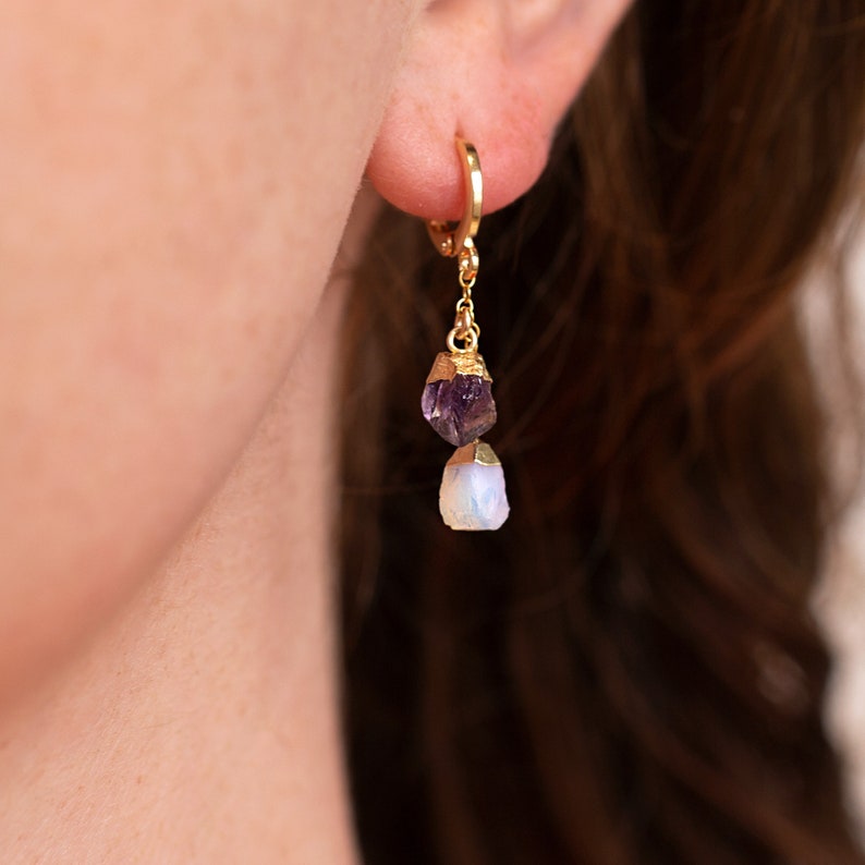 May include: Gold hoop earrings with a dangling amethyst and moonstone crystal. The crystals are raw and have a natural, irregular shape.