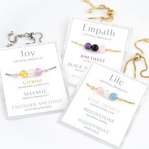 May include: A selection of crystal bracelets with gemstone beads, presented on cards. The bracelets are labelled "Joy," "Empath," and "Life." Each bracelet features a different combination of stones, including citrine, amethyst, rose quartz, and aquamarine. The cards list the properties of each stone.