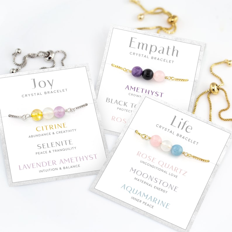 May include: A selection of crystal bracelets with gemstone beads, presented on cards. The bracelets are labelled "Joy," "Empath," and "Life." Each bracelet features a different combination of stones, including citrine, amethyst, rose quartz, and aquamarine. The cards list the properties of each stone.