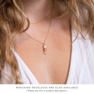 May include: A gold chain necklace with a pendant made of three small beads. The beads are white, orange, and pink.