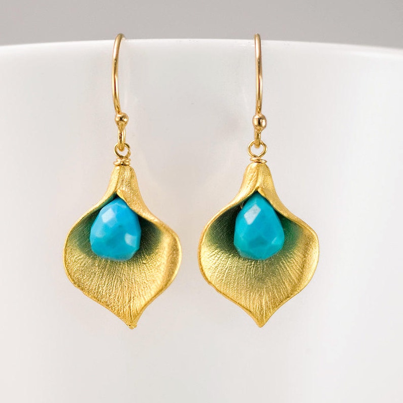 May include: Gold earrings with a turquoise gemstone in the shape of a teardrop, set in a gold flower design.