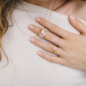 May include: A gold necklace with a pink stone pendant and a small leaf charm. A matching pink stone ring is on the finger of a hand.