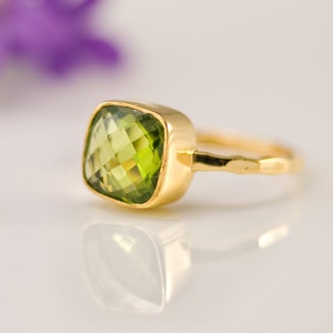 May include: A gold ring with a large, square, green peridot gemstone. The ring band is textured and has a hammered finish.