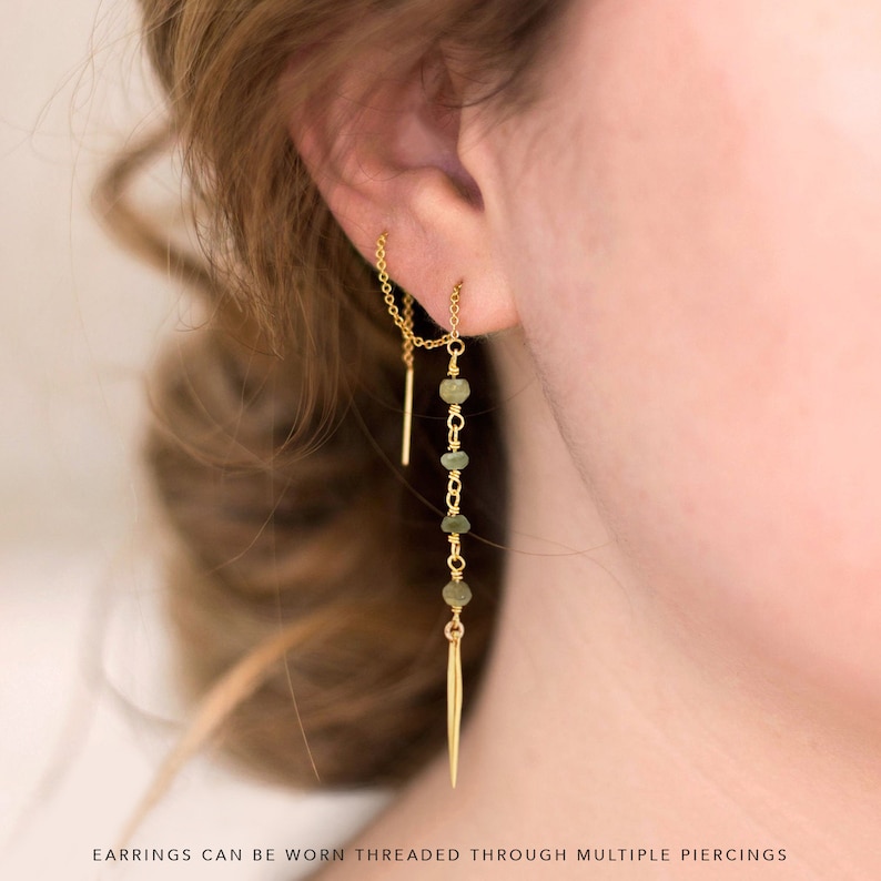 K&ouml;nnte beinhalten: Goldfarbene Ohrringe mit Ketten-Design. Die Ohrringe haben einen vertikalen Stab, kleine gr&uuml;ne Perlen und ein spitzes Ende. Der Text im Bild lautet: "EARNINGS CAN BE WORN THREADED THROUGH MULTIPLE PIERCINGS."