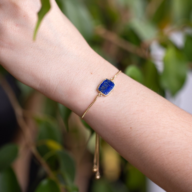 Pu&ograve; includere: Un braccialetto a catena dorata con un ciondolo in lapislazzuli blu. Il braccialetto &egrave; regolabile e ha una catena delicata.