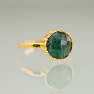 K&ouml;nnte beinhalten: Ein goldener Ring mit einem dunkelgr&uuml;nen Edelstein. Der Ring hat eine schlichte Band und der Edelstein ist in einer Zargenfassung gefasst.