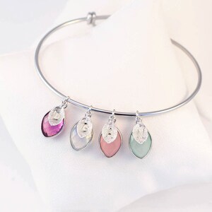 May include: A silver bangle bracelet with four charms. Each charm is a silver leaf with a letter on it and a gemstone in the center. The gemstones are pink, green, white, and purple.