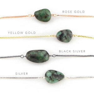 May include: Four emerald green gemstone necklaces with different chain styles: rose gold, yellow gold, black silver, and silver.