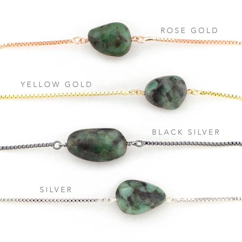 May include: Four emerald green gemstone necklaces with different chain styles: rose gold, yellow gold, black silver, and silver.