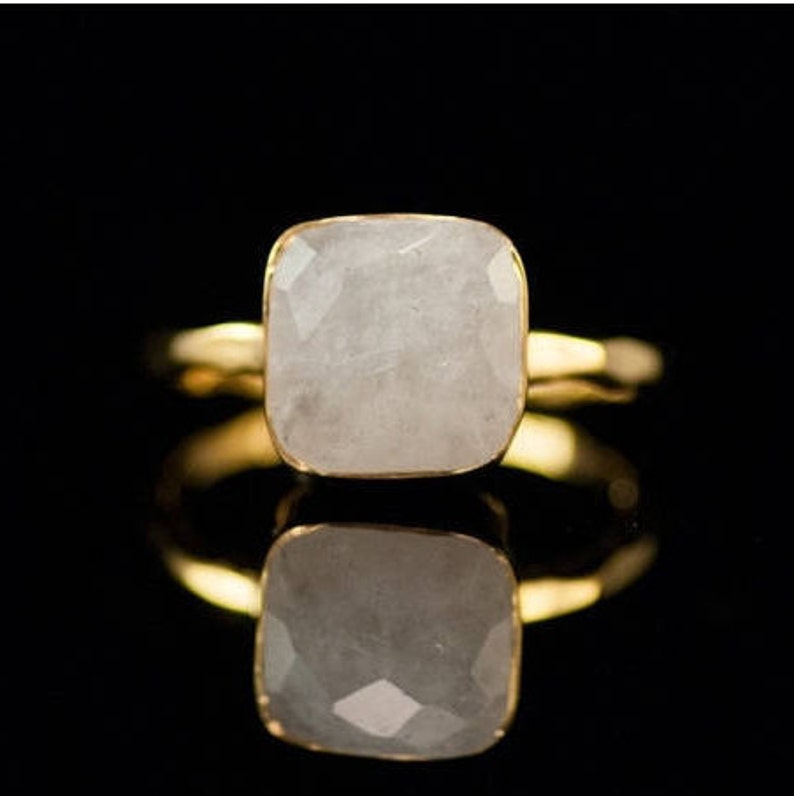 May include: A gold ring with a white square-shaped gemstone.