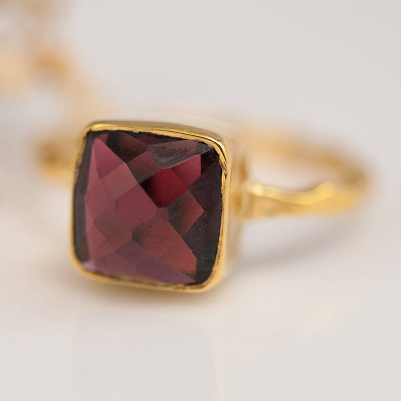May include: A gold ring with a square, faceted, dark purple gemstone.