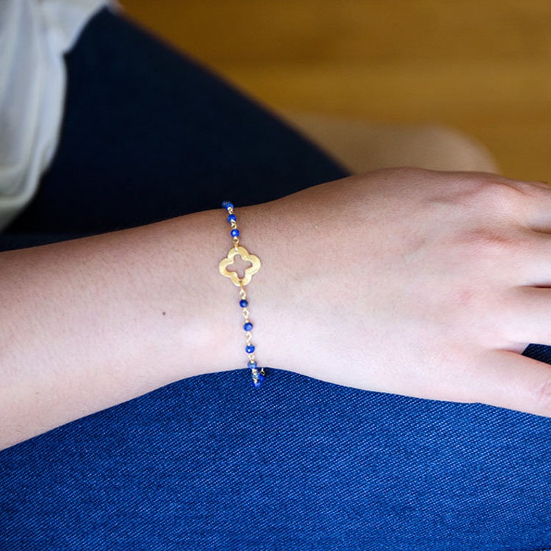 May include: A gold bracelet with a four-leaf clover charm and blue beads.