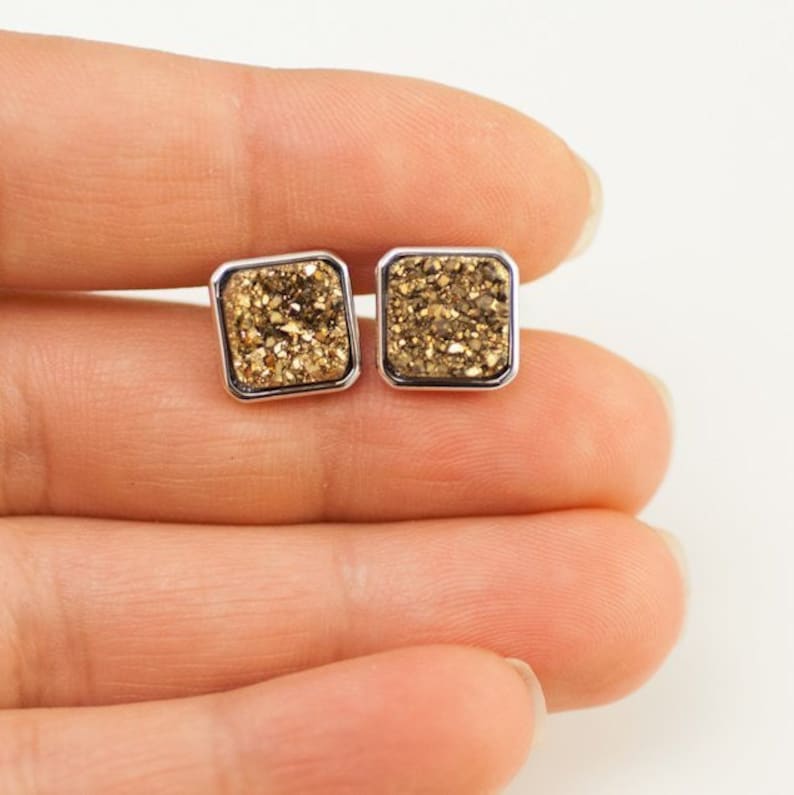 May include: A pair of gold and silver square stud earrings with a sparkly, glittery finish.