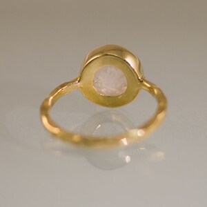 May include: A gold ring with a white gemstone set in a bezel setting. The ring band is textured and has a hammered finish.