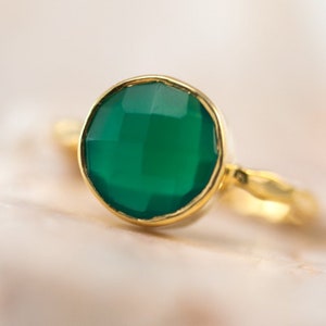 May include: A gold ring with a green gemstone. The ring has a simple band and a round, faceted stone.