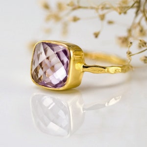 May include: A gold ring with a square-shaped amethyst gemstone. The ring has a textured band.
