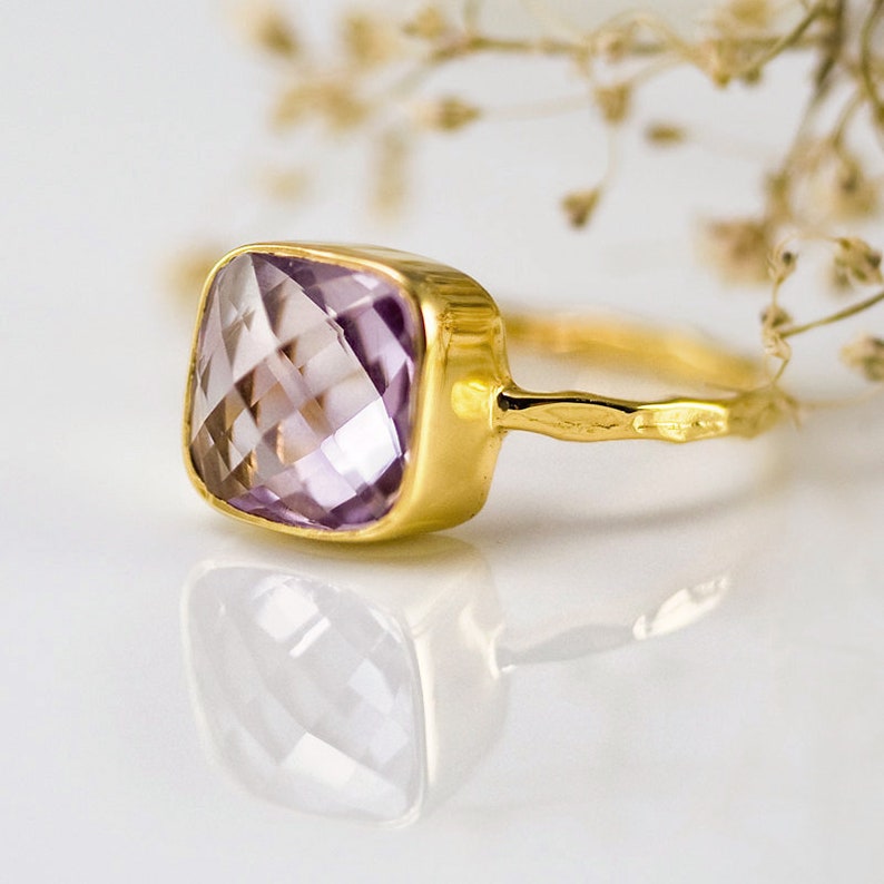May include: A gold ring with a square-shaped amethyst gemstone. The ring has a textured band.