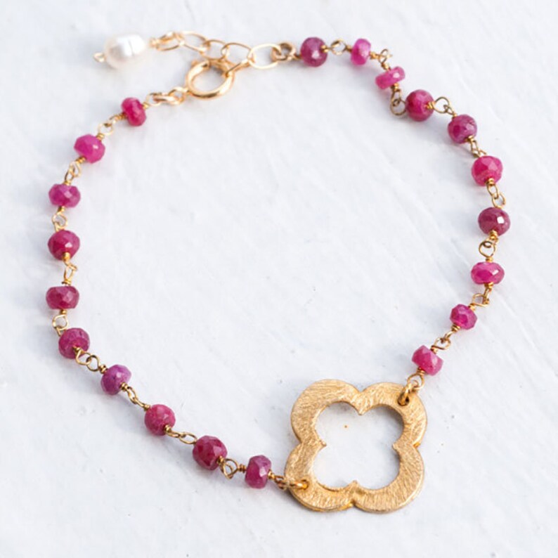 May include: A gold bracelet with a four-leaf clover charm and pink beads.