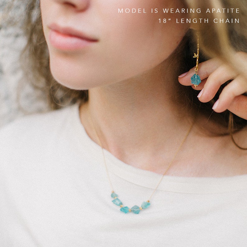 May include: A gold necklace with a row of light blue apatite stones. The model is wearing an 18 inch apatite chain.
