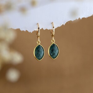 May include: A pair of gold earrings with dark green gemstone drops. The earrings have a simple hoop design.