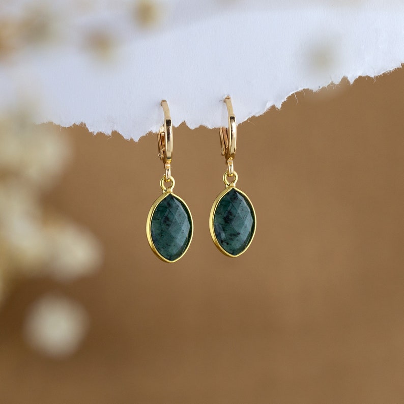 May include: A pair of gold earrings with dark green gemstone drops. The earrings have a simple hoop design.