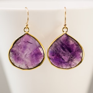 May include: A pair of gold-toned earrings with large, teardrop-shaped amethyst stones.