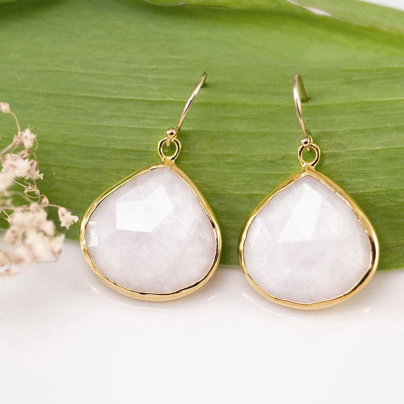 May include: A pair of gold earrings with white teardrop-shaped stones.