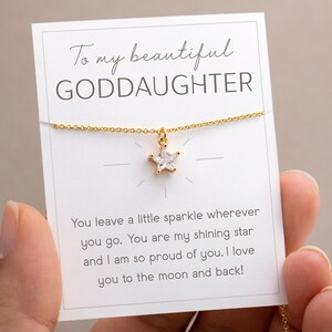 Puede incluir: Un collar dorado con un colgante en forma de estrella, presentado en una tarjeta blanca. La tarjeta tiene el texto "To my beautiful GODDAUGHTER" y un mensaje cari&ntilde;oso. El collar es sostenido por una persona.
