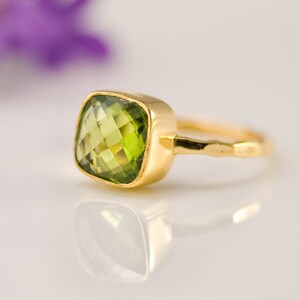 Pu&ograve; includere: Un anello d'oro con una pietra preziosa verde chiaro a taglio quadrato. L'anello ha un design semplice ed elegante con una fascia liscia e lucida e un'incastonatura a castone. Le sfaccettature della pietra preziosa catturano la luce, creando un effetto scintillante.
