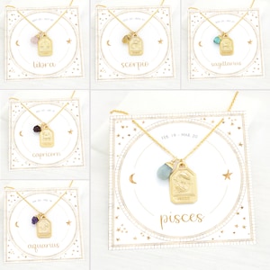 May include: Gold zodiac necklace with a gemstone charm and a gold tag with the zodiac symbol and name. The necklaces are displayed on white cards with a gold circle and stars. The cards also include the zodiac dates.
