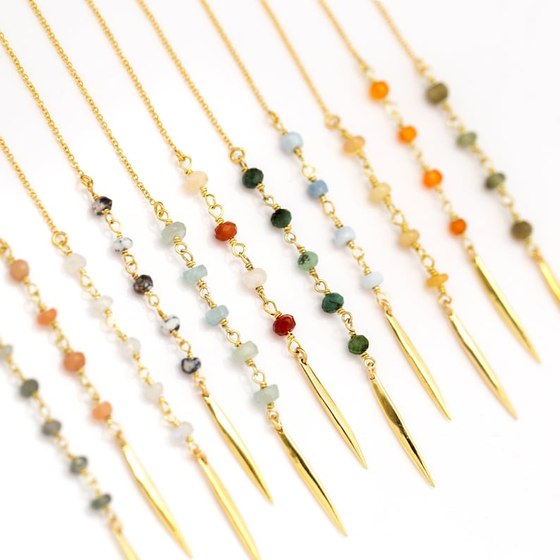 K&ouml;nnte beinhalten: Eine Sammlung zarter, goldfarbener Kettenohrringe. Jeder Ohrring hat eine Kette aus bunten Edelsteinen und einen langen, spitz zulaufenden Goldanh&auml;nger. Die Edelsteine sind in verschiedenen Farben gehalten, darunter Gr&uuml;n, Blau, Orange und Wei&szlig;.