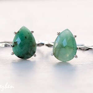 May include: Two silver rings with teardrop-shaped green gemstones. The rings are on a white surface.