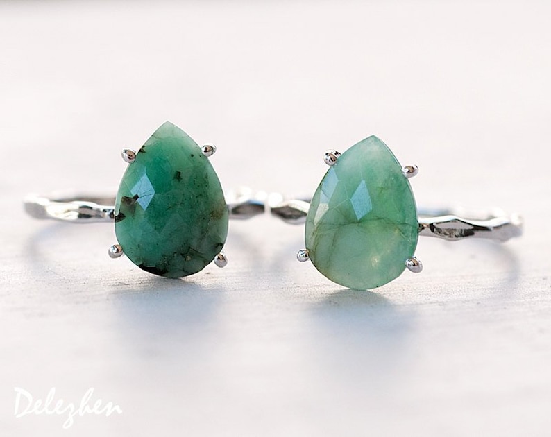 May include: Two silver rings with teardrop-shaped green gemstones. The rings are on a white surface.