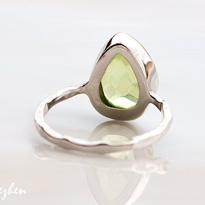 May include: A silver ring with a pear-shaped green gemstone set in a bezel setting. The ring band is textured and has a hammered finish.