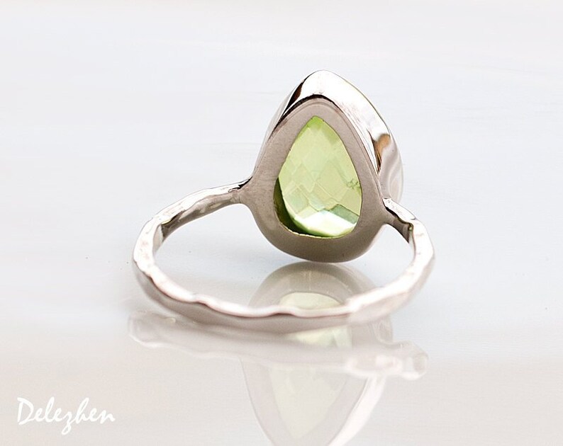 May include: A silver ring with a pear-shaped green gemstone set in a bezel setting. The ring band is textured and has a hammered finish.