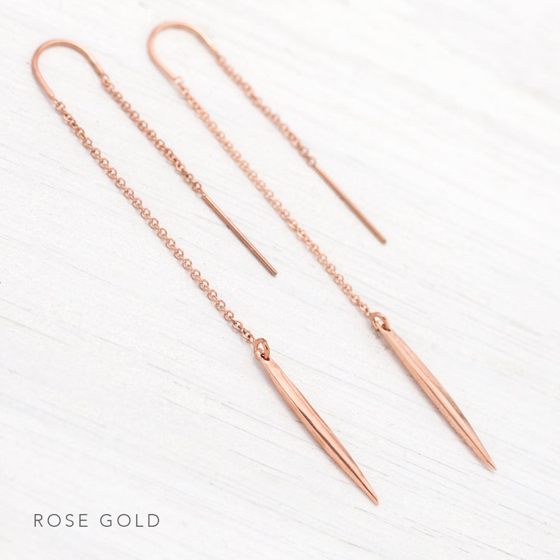 Op de afbeelding: Oorbellen van ros&eacute;goud met een dunne ketting en een puntige, langwerpige druppel.  ROSE GOLD staat in de linkerbenedenhoek van de afbeelding.