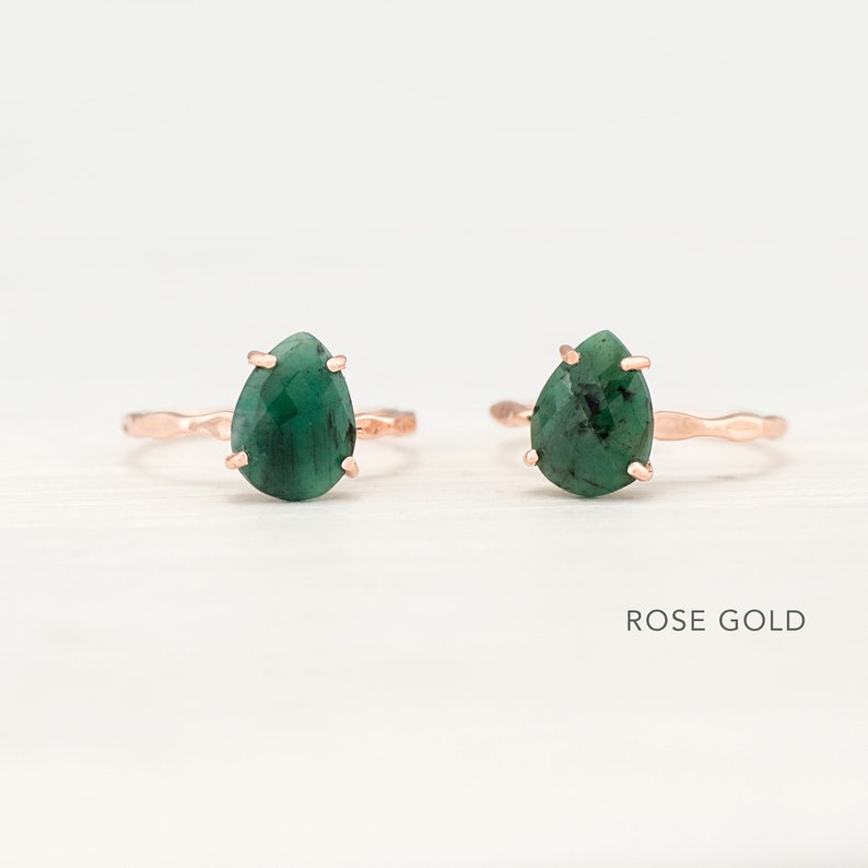 May include: Two rose gold rings with green gemstone pear-shaped settings. The rings have a hammered texture. ROSE GOLD text is visible below the rings.
