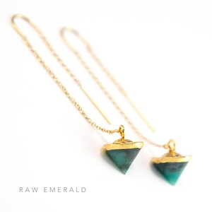 May include: A pair of gold chain earrings with a raw emerald gemstone pendant. The emerald is a dark green color and has a triangular shape.