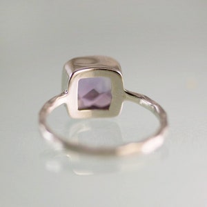 May include: A silver ring with a square, purple gemstone. The ring band is textured.