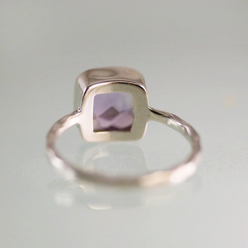 May include: A silver ring with a square, purple gemstone. The ring band is textured.