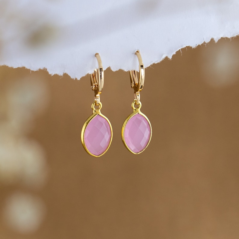 May include: A pair of gold hoop earrings with pink oval-shaped gemstones.