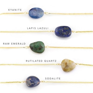 May include: Five gold chains with different gemstones hanging from them. The gemstones are: Kyanite, Lapis Lazuli, Raw Emerald, Rutilated Quartz, and Sodalite.