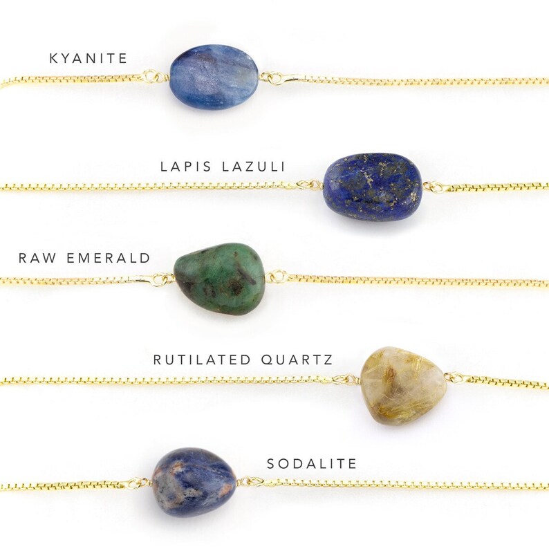 May include: Five gold chains with different gemstones hanging from them. The gemstones are: Kyanite, Lapis Lazuli, Raw Emerald, Rutilated Quartz, and Sodalite.
