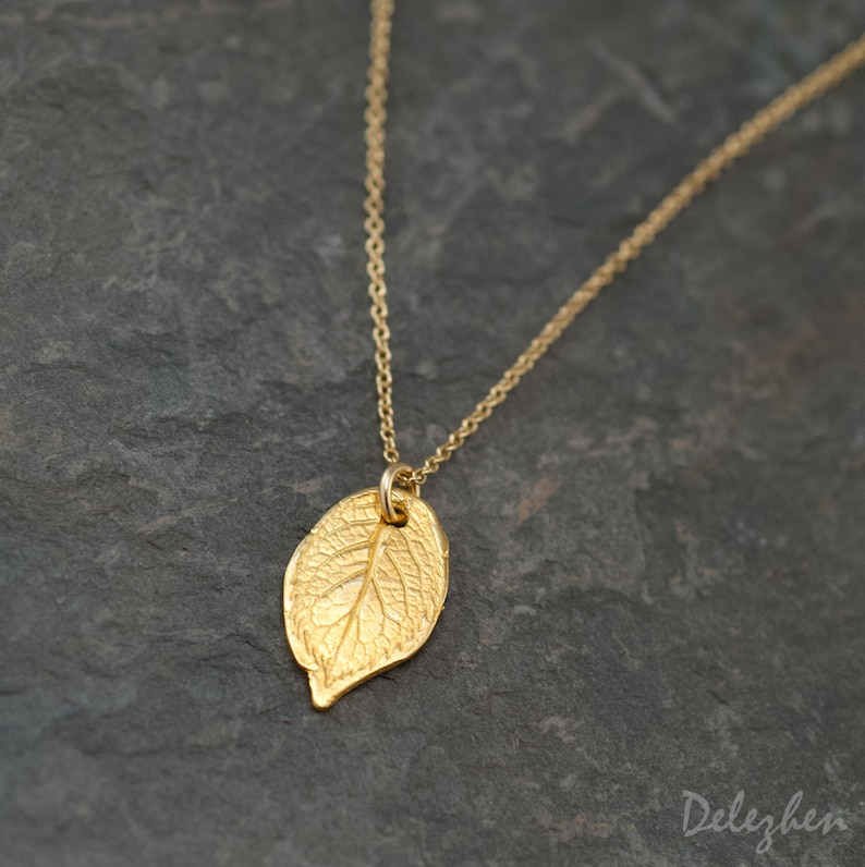May include: A gold leaf pendant necklace on a gold chain. The leaf is detailed with veins and has a smooth, polished finish.