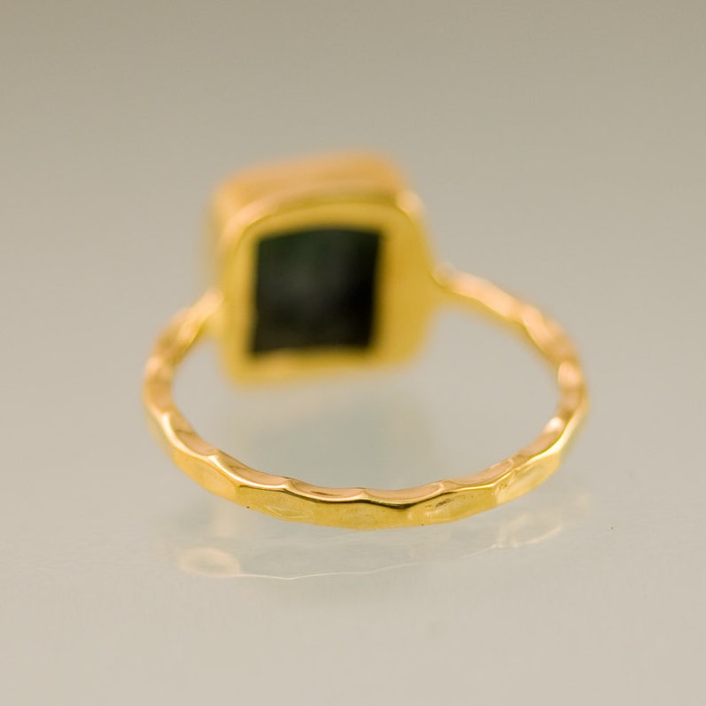 Pode incluir: Um anel de ouro com uma pedra preciosa verde quadrada engastada em uma banda martelada.